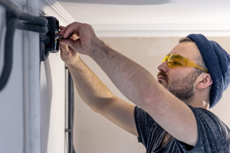 An electrician is mounting electric sockets on the white wall indoors.