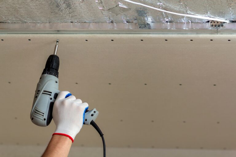 Worker hand with screwdriver connecting suspended drywall ceiling to metal frame. Renovation